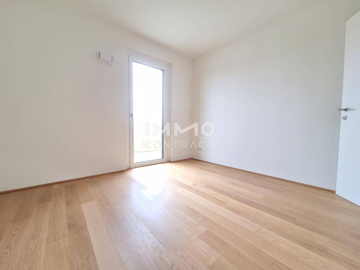 Heller, leerer Raum mit Parkettboden und Zugang zu einem Balkon.