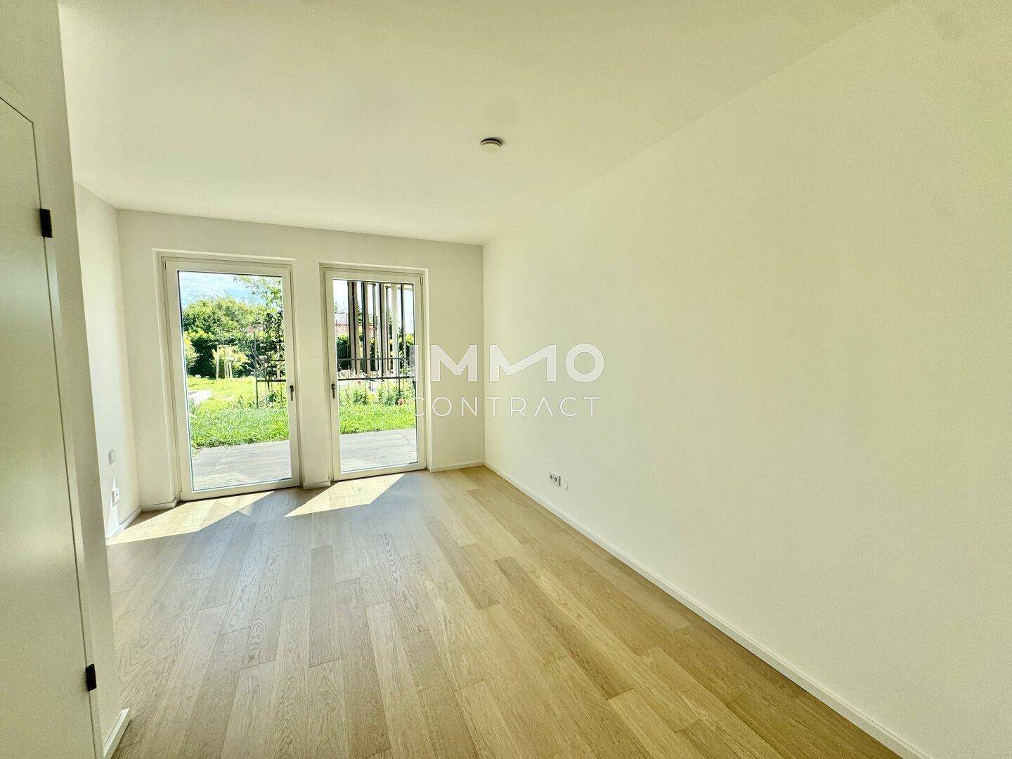 Helles Zimmer mit Holzboden und großen Fenstern, die den Blick ins Grüne freigeben.
