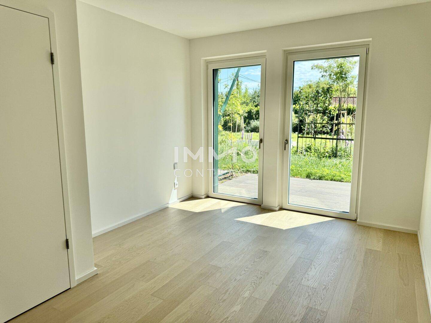 Helles Zimmer mit Holzboden und Zugang zu einem kleinen Außenbereich.