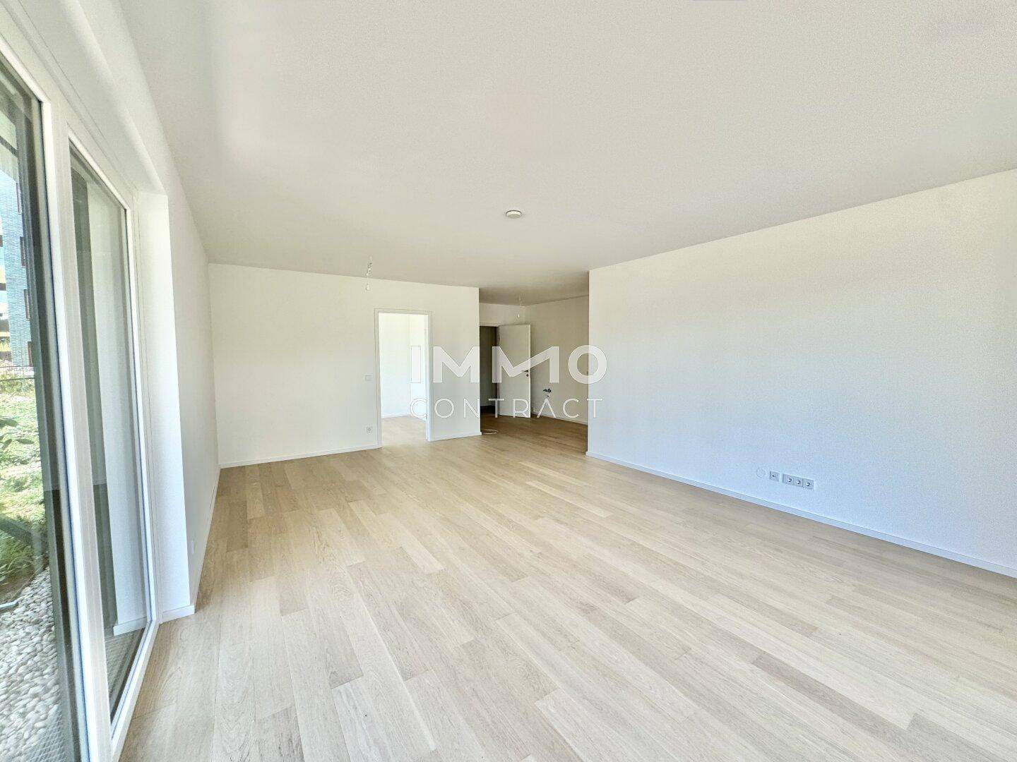 Heller, geräumiger Wohnbereich mit Holzboden und viel Tageslicht durch große Fenster.