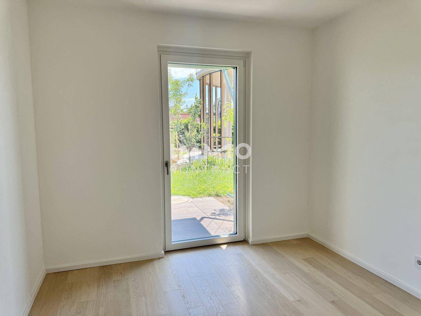 Helles Zimmer mit Holzboden und direktem Zugang zu einem kleinen Außenbereich.