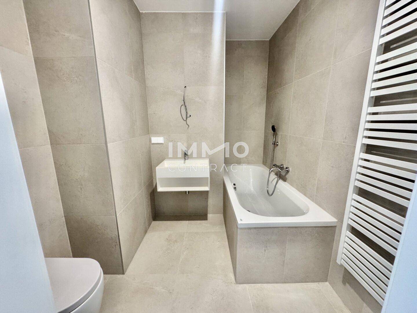 Modernes Badezimmer mit Badewanne, WC, Waschbecken und Handtuchheizkörper.