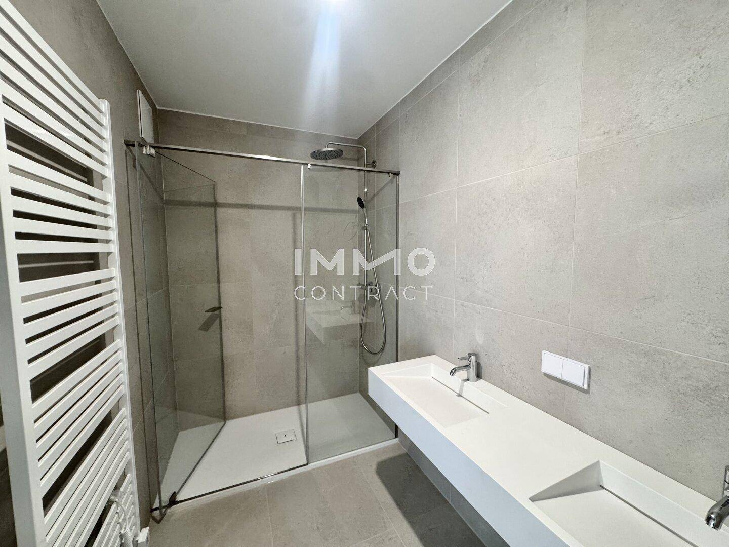 Modernes Badezimmer mit großer begehbarer Dusche, Wandheizkörper und minimalistischem Doppelwaschbecken.