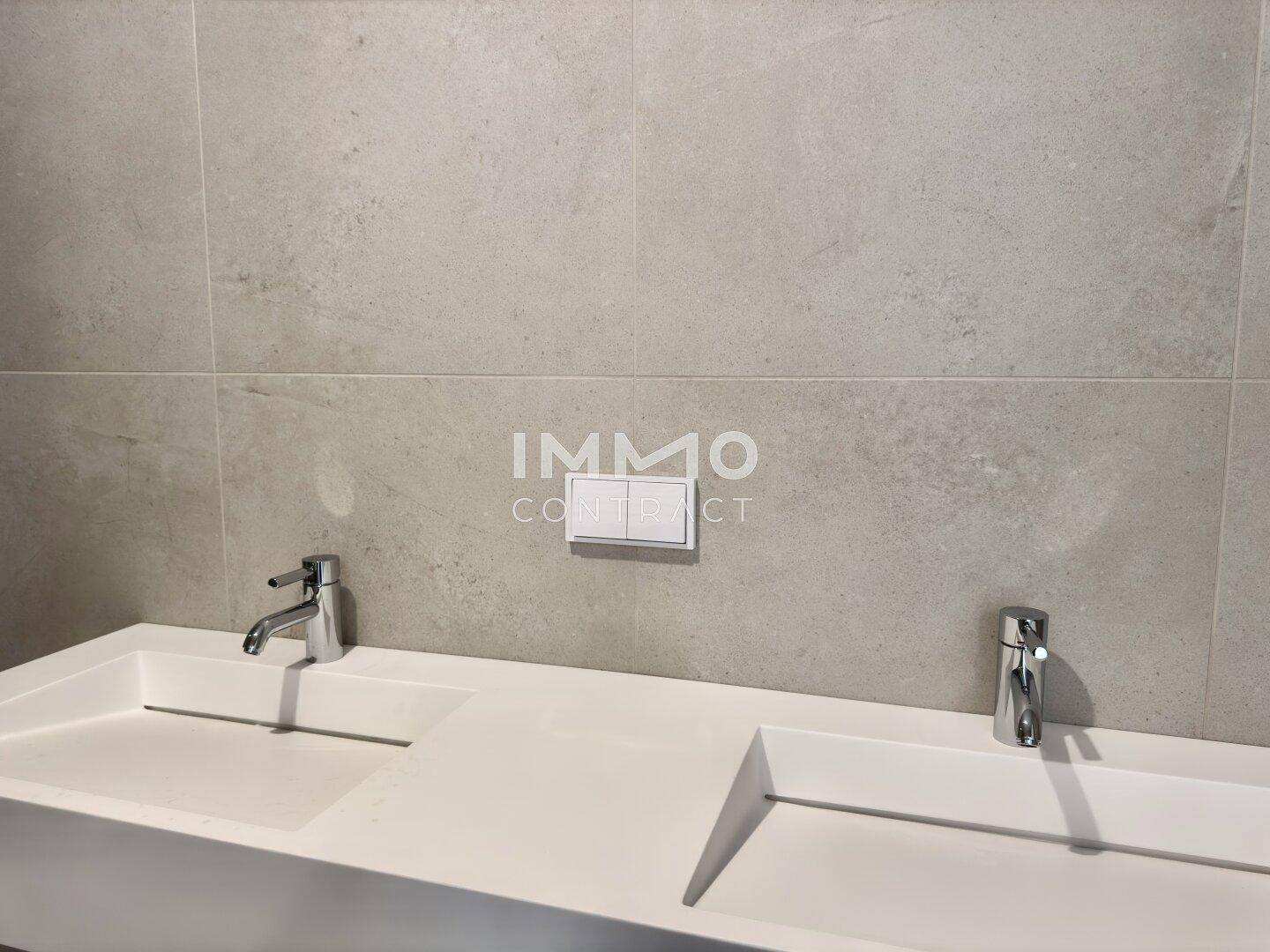 Modernes Doppelwaschbecken mit zwei Armaturen und großformatigen Fliesen an der Wand.