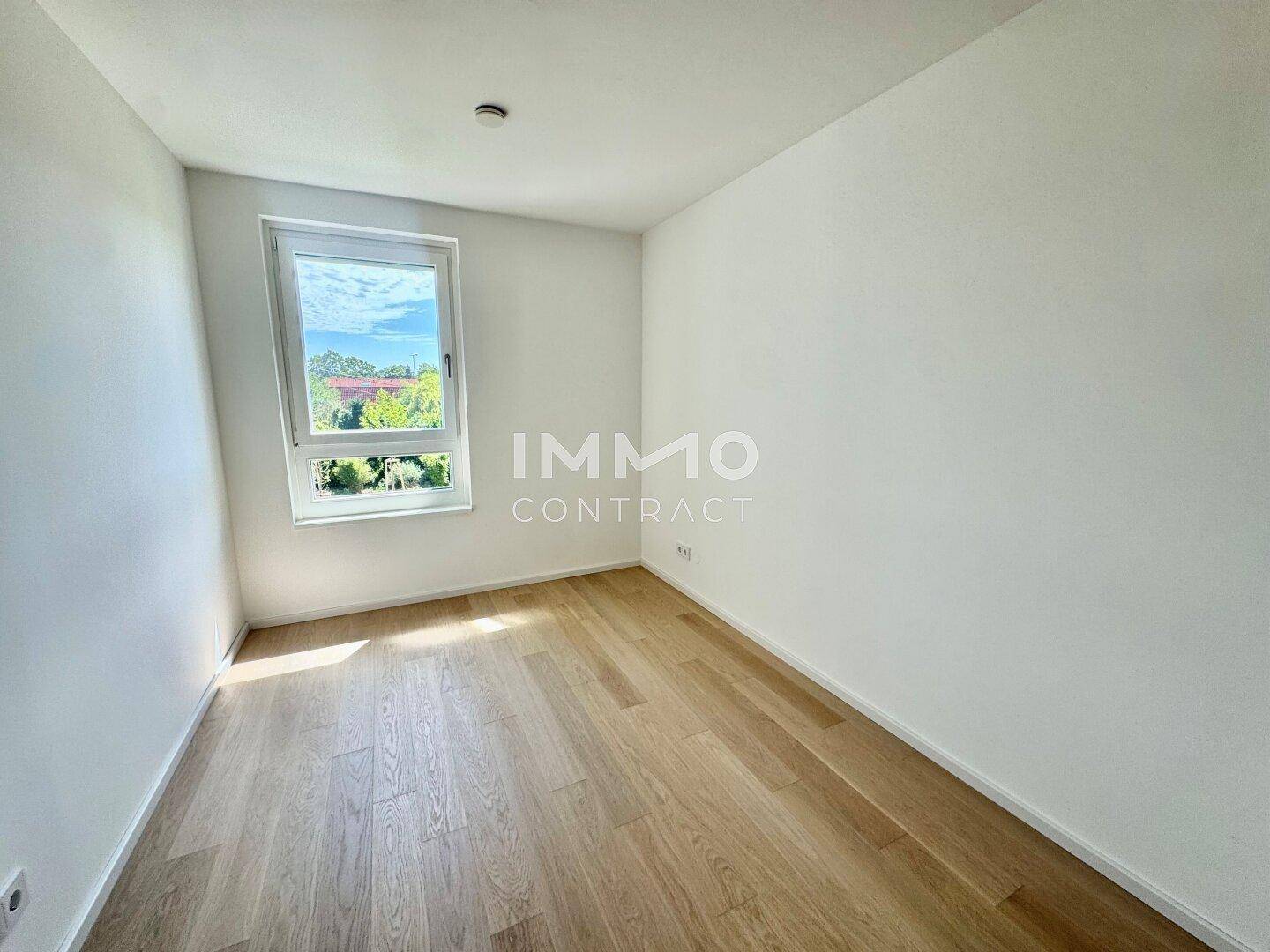 Helles, leeres Zimmer mit großem Fenster und hellem Holzparkettboden.