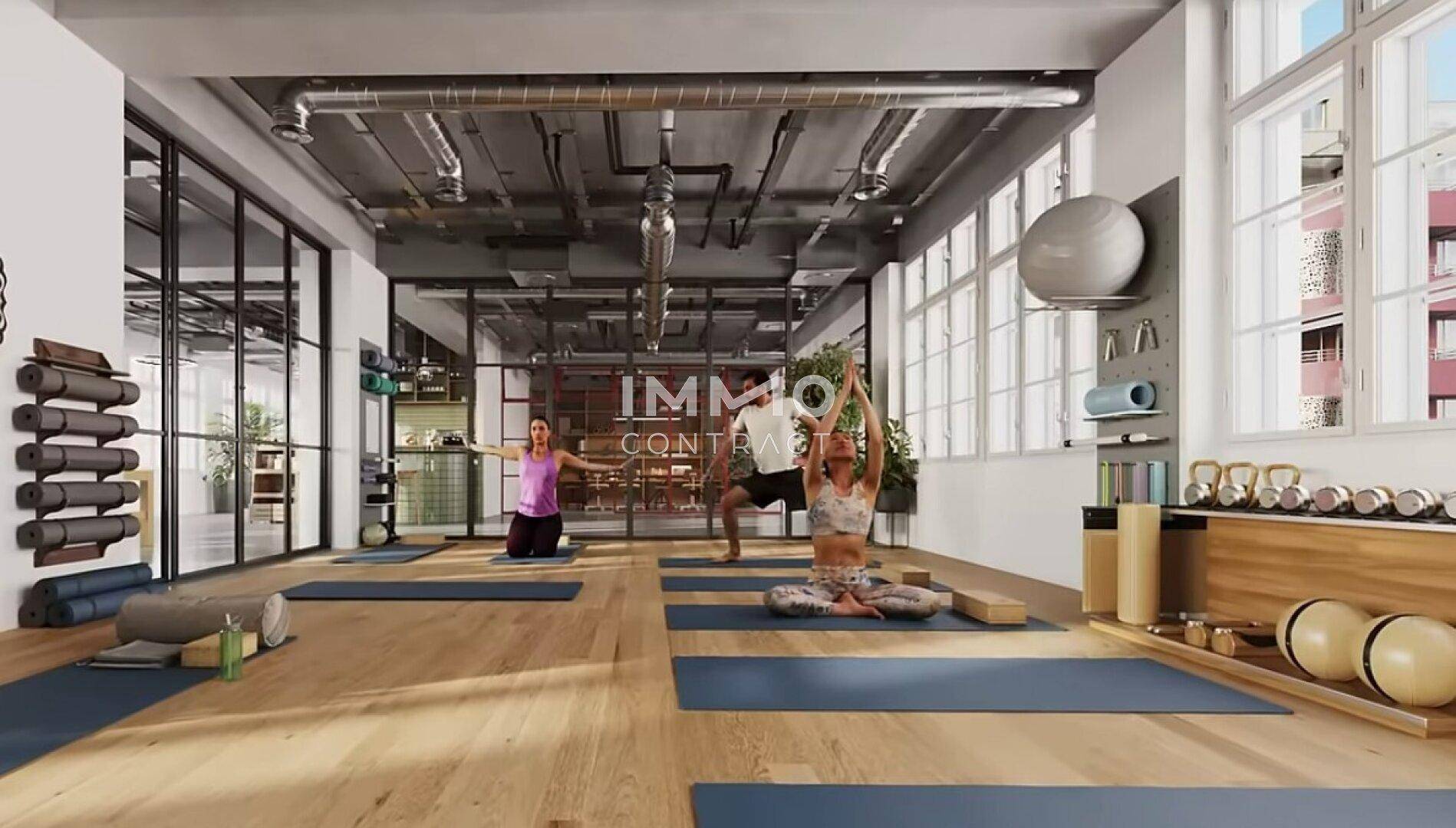 Geräumiger Fitnessraum mit Holzboden, Yogamatten und Sportgeräten in modernem Ambiente.