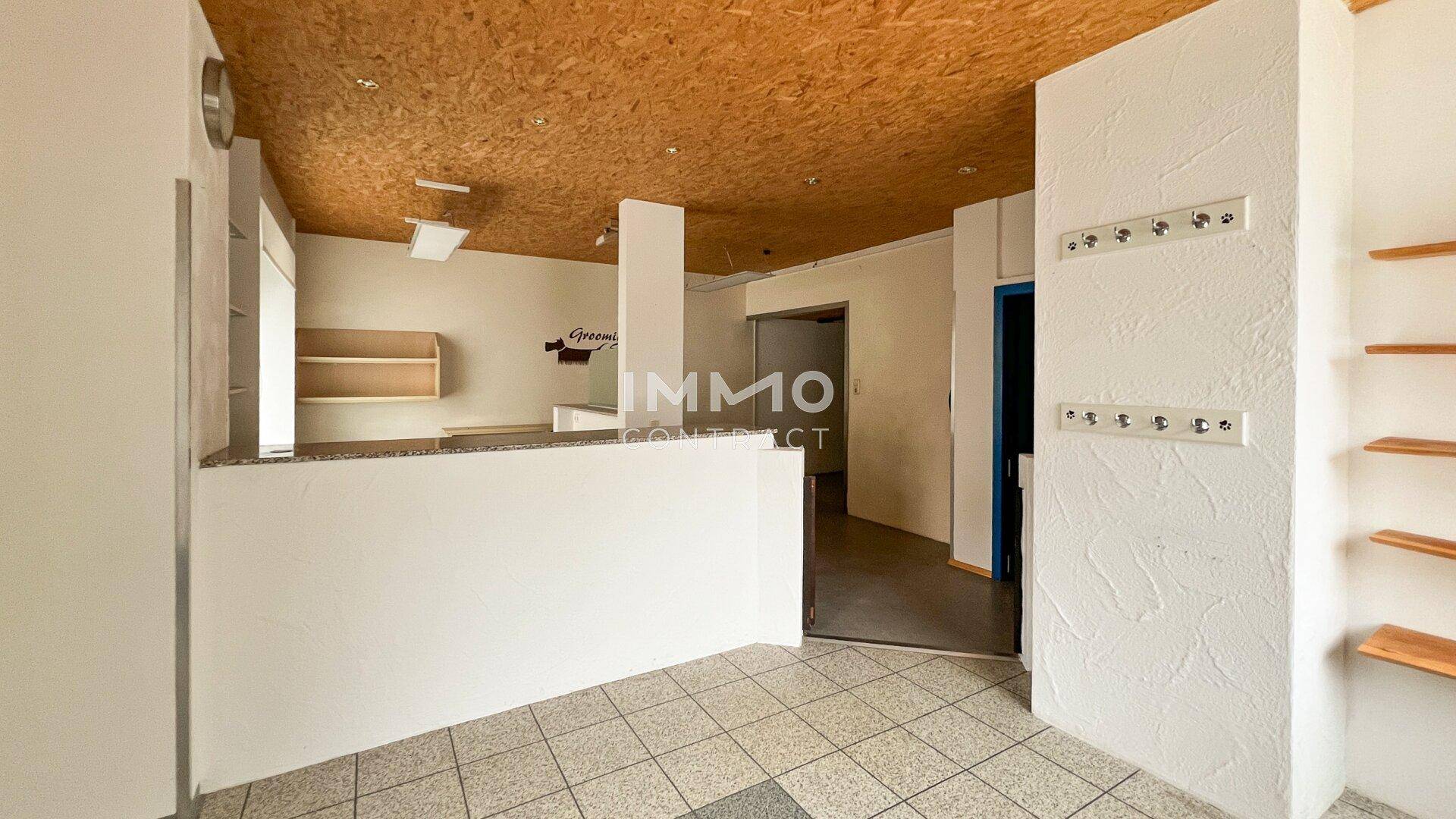 Innenraum eines Gewerbeobjekts mit gefliestem Boden, einer Theke und einer Decke aus Holzspanplatten.