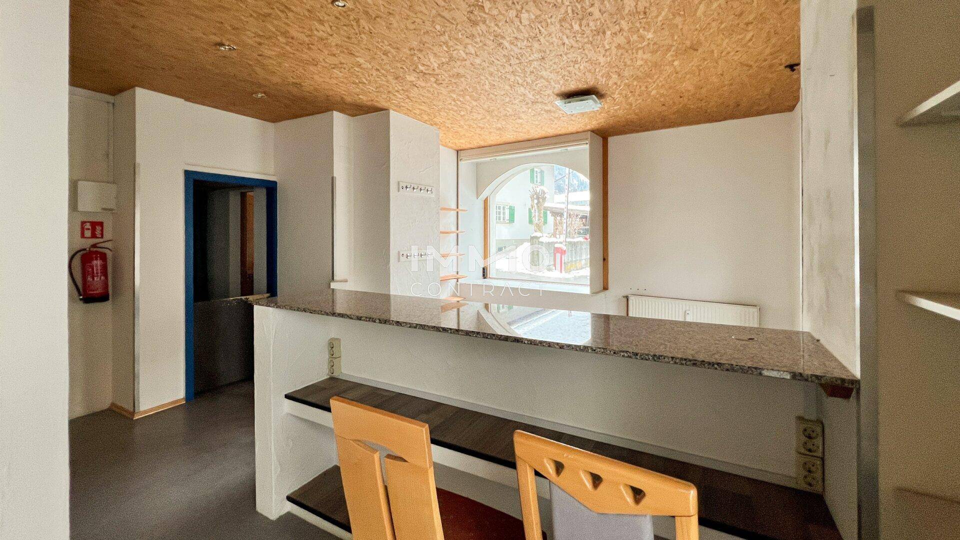 Thekenbereich in einem Gewerberaum mit Granitplatte, Holzregalen und Blick nach draußen durch ein großes Fenster.