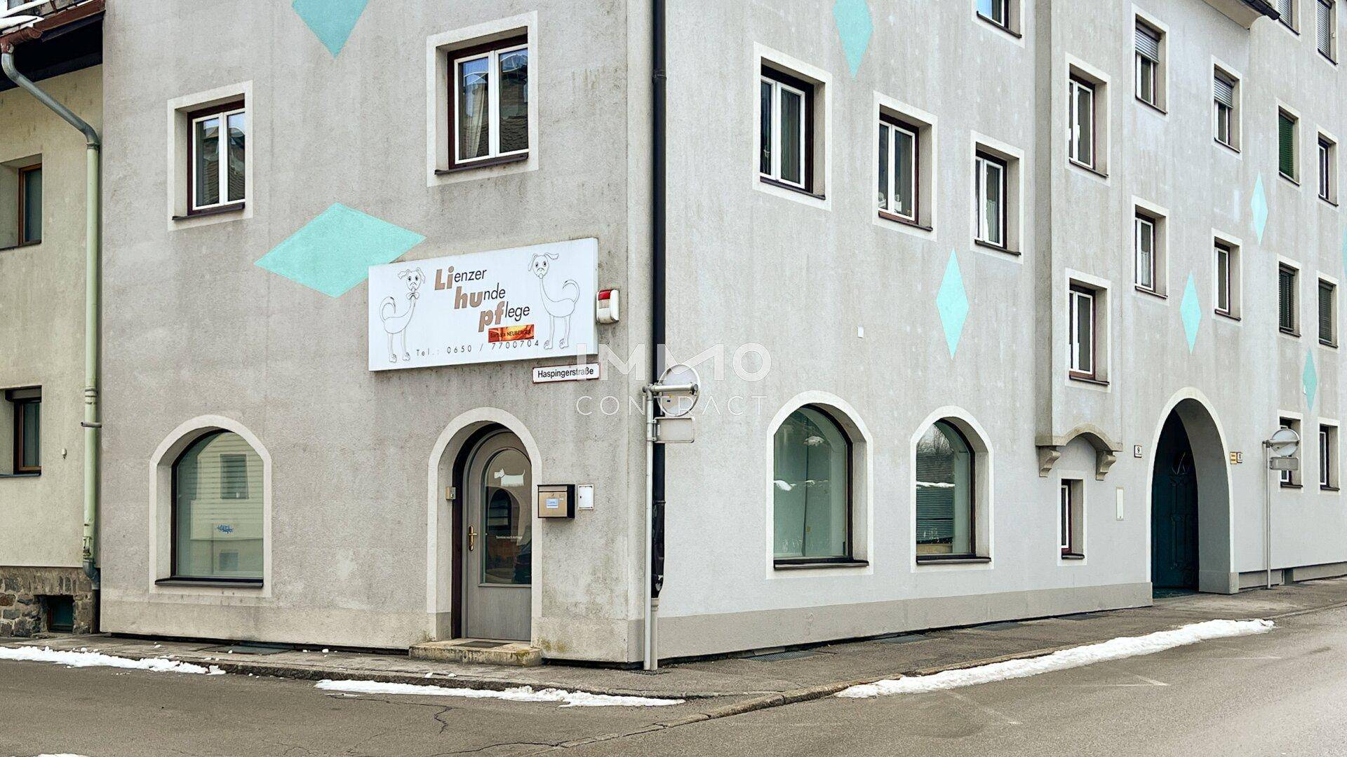 Nahaufnahme der Gebäudefassade mit runden Fenstern im Erdgeschoss und einem Geschäftsschild an der Ecke.