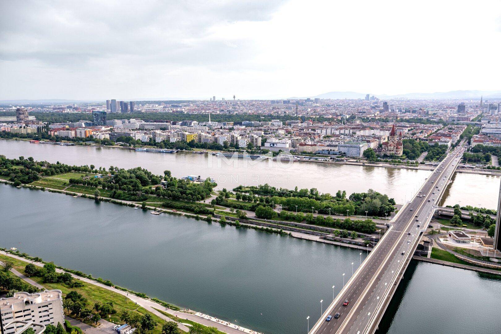 Luftaufnahme einer Stadt mit Fluss, Brücke und dichter Bebauung unter bewölktem Himmel, eine weite Perspektive.