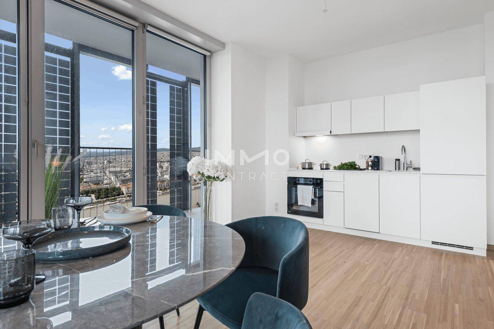 Moderne offene Küche mit weißen Schränken, Essbereich und weitem Stadtblick durch große Fenster.