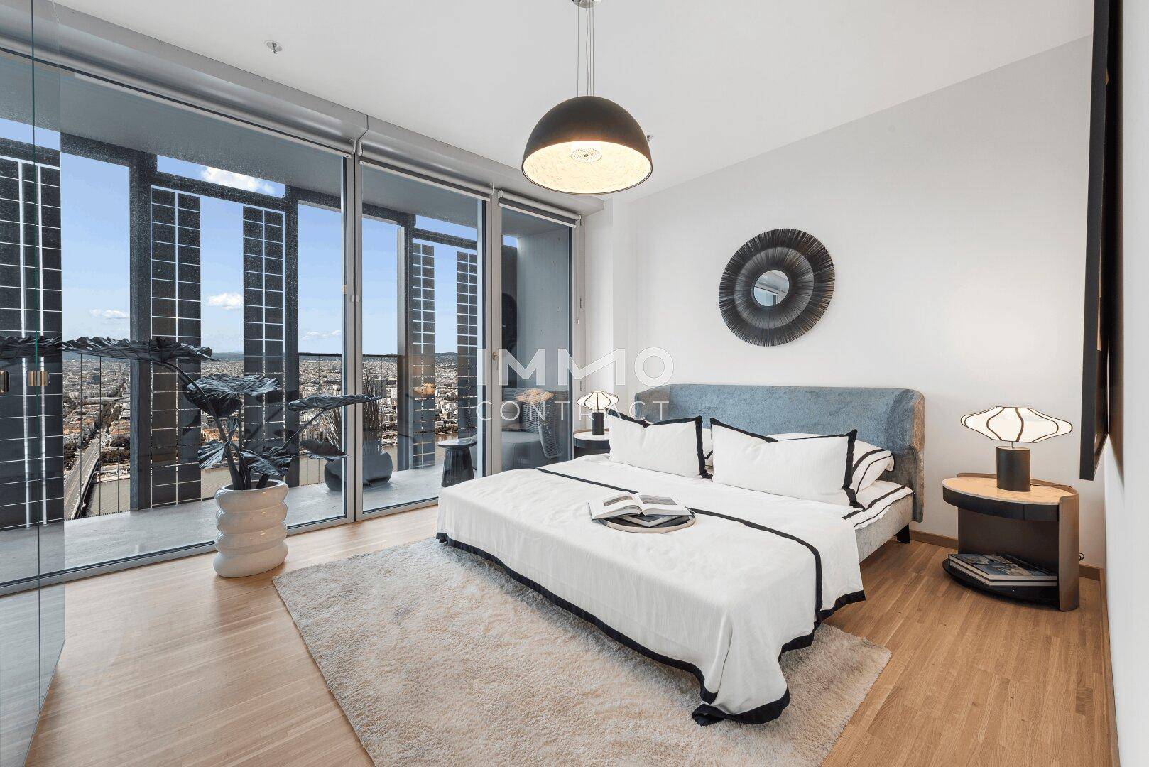 Helles Schlafzimmer mit Doppelbett, Holzboden und Zugang zu einem Balkon mit Stadtblick.