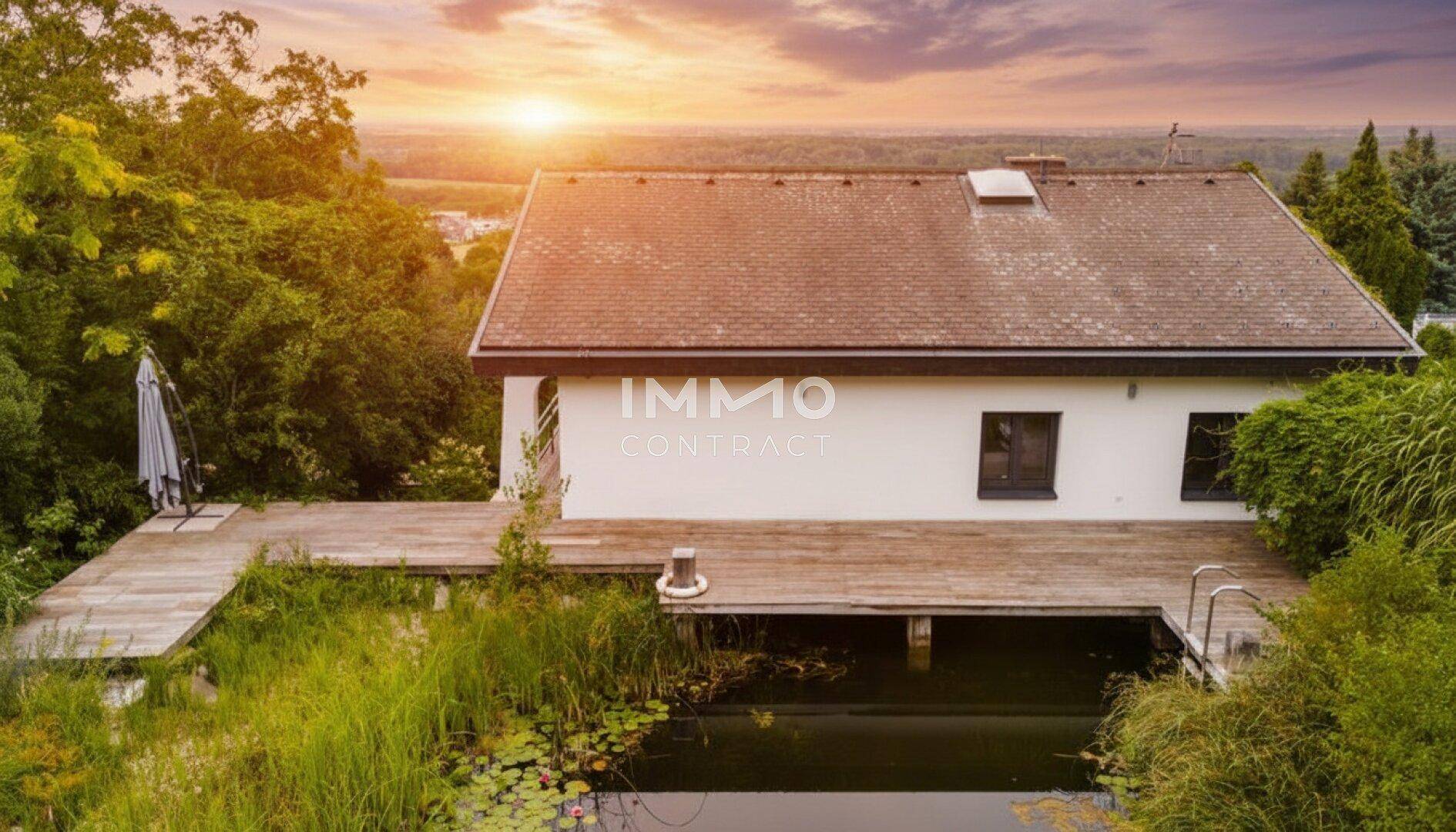 Hausfassade mit großem Naturpool und Holzdeck bei Sonnenuntergang, umgeben von Grün.