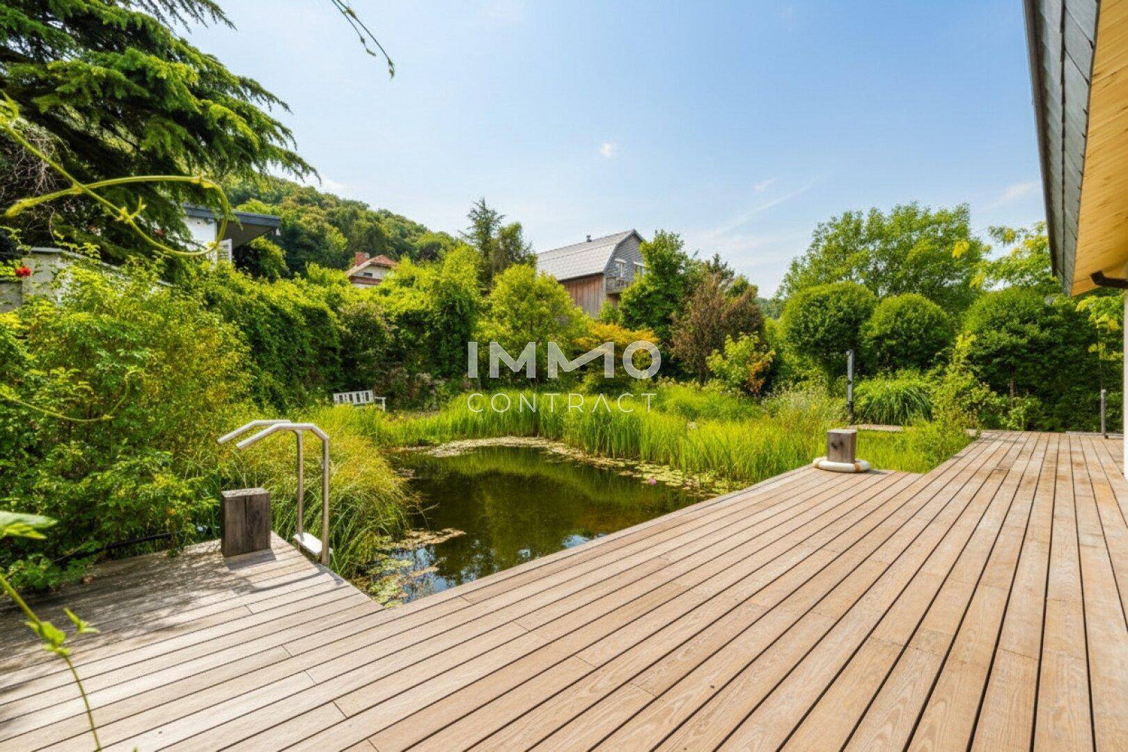 Idyllischer Naturpool mit Holzdeck und üppiger Bepflanzung, ideal zum Entspannen.