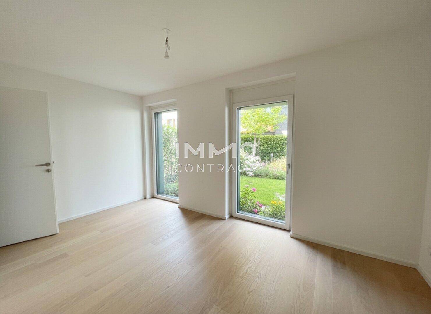 Leeres Zimmer mit hellem Parkettboden und Zugang zum Garten, bietet einen ruhigen Ausblick ins Grüne.