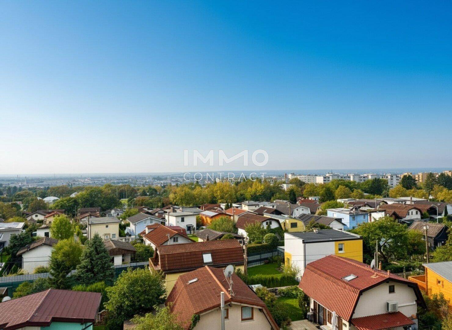 Weitläufiger Blick über eine Wohnsiedlung mit vielen Häusern und grünen Bäumen unter blauem Himmel.