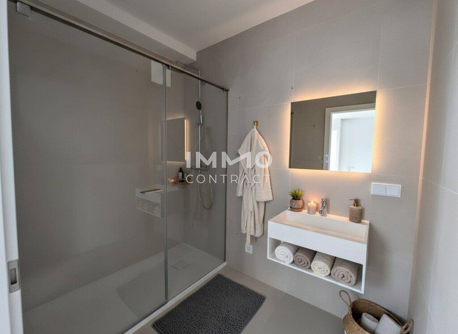 Modernes Badezimmer mit großer begehbarer Dusche, Wandwaschbecken und beleuchtetem Spiegel.
