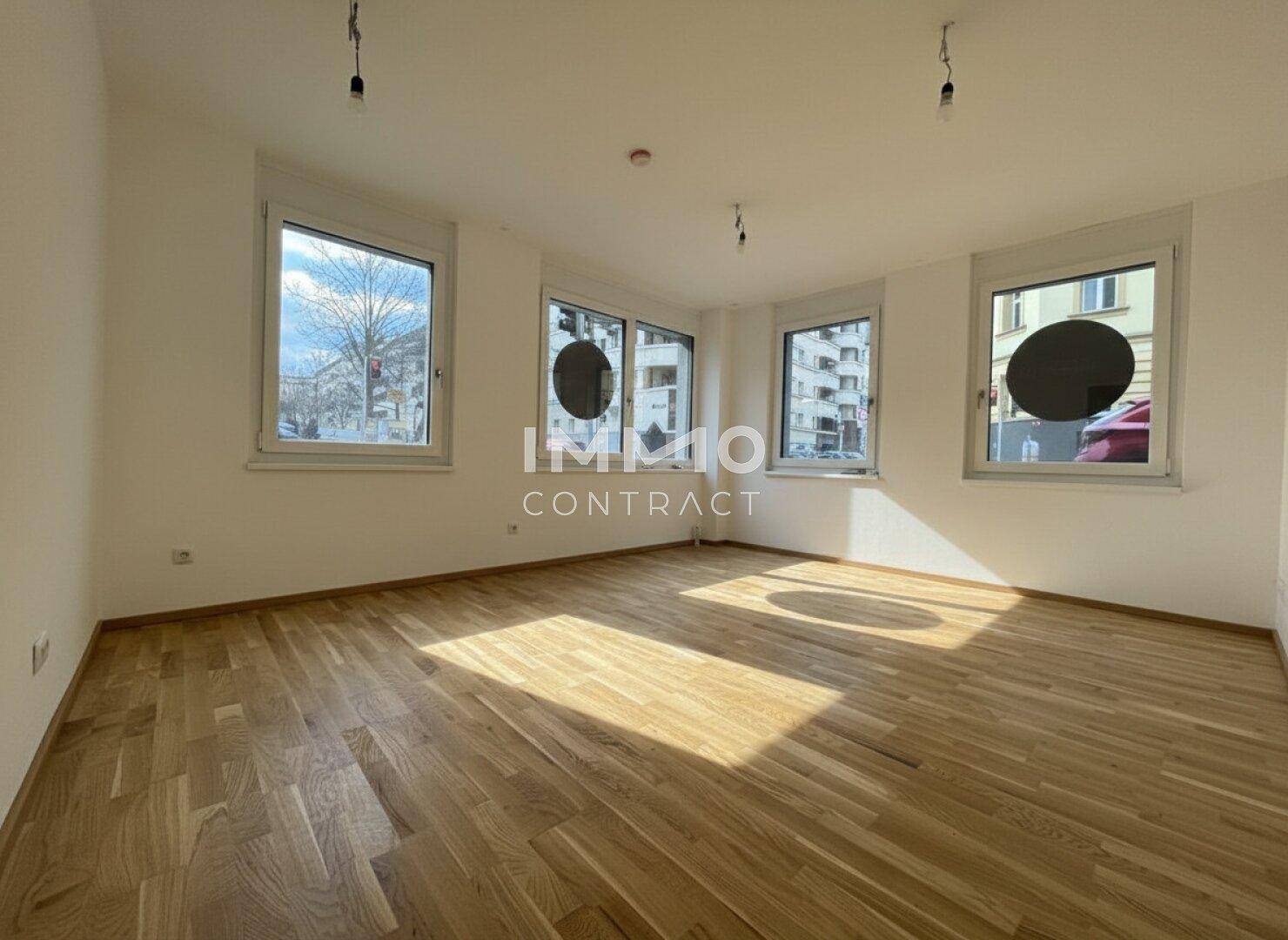 Heller, leerer Raum mit Holzboden und mehreren Fenstern, die viel Tageslicht hereinlassen und eine offene Atmosphäre schaffen.