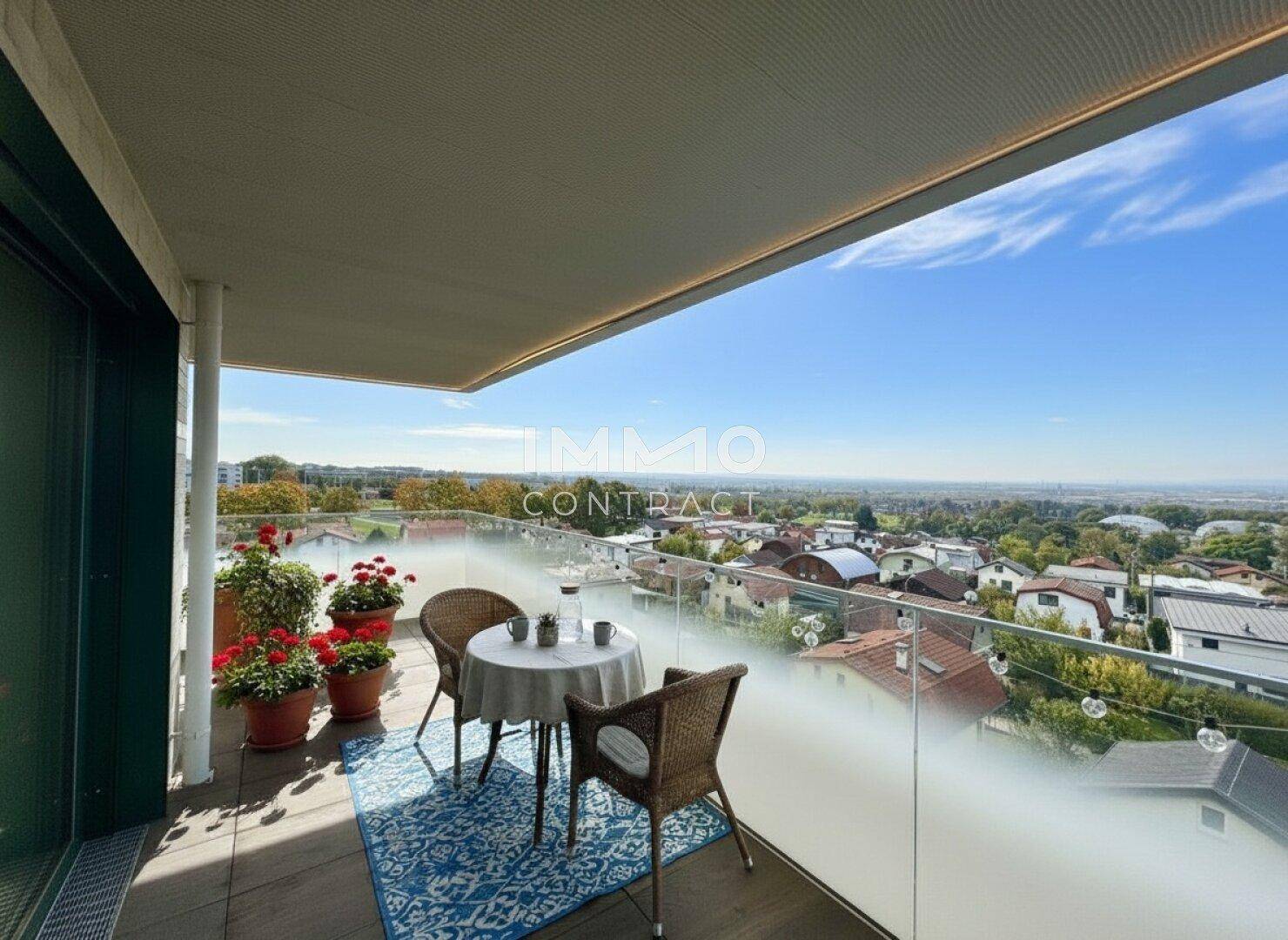Möblierter Balkon mit Glasgeländer und weitem Blick über die Stadt und die grüne Landschaft.