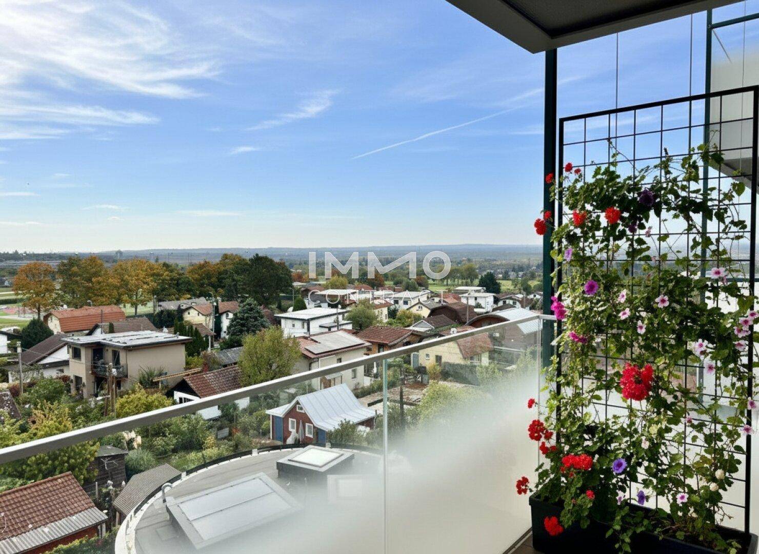 Heller Balkon mit Pflanzen und einem weiten Blick über die umliegende Wohngegend und Landschaft.