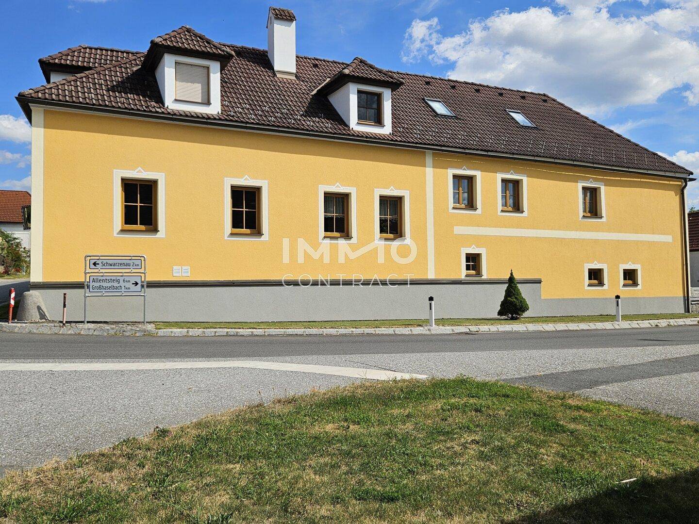 Gelbe Fassade eines traditionellen Gebäudes mit braunem Dach und Gaubenfenstern an einer Straße.