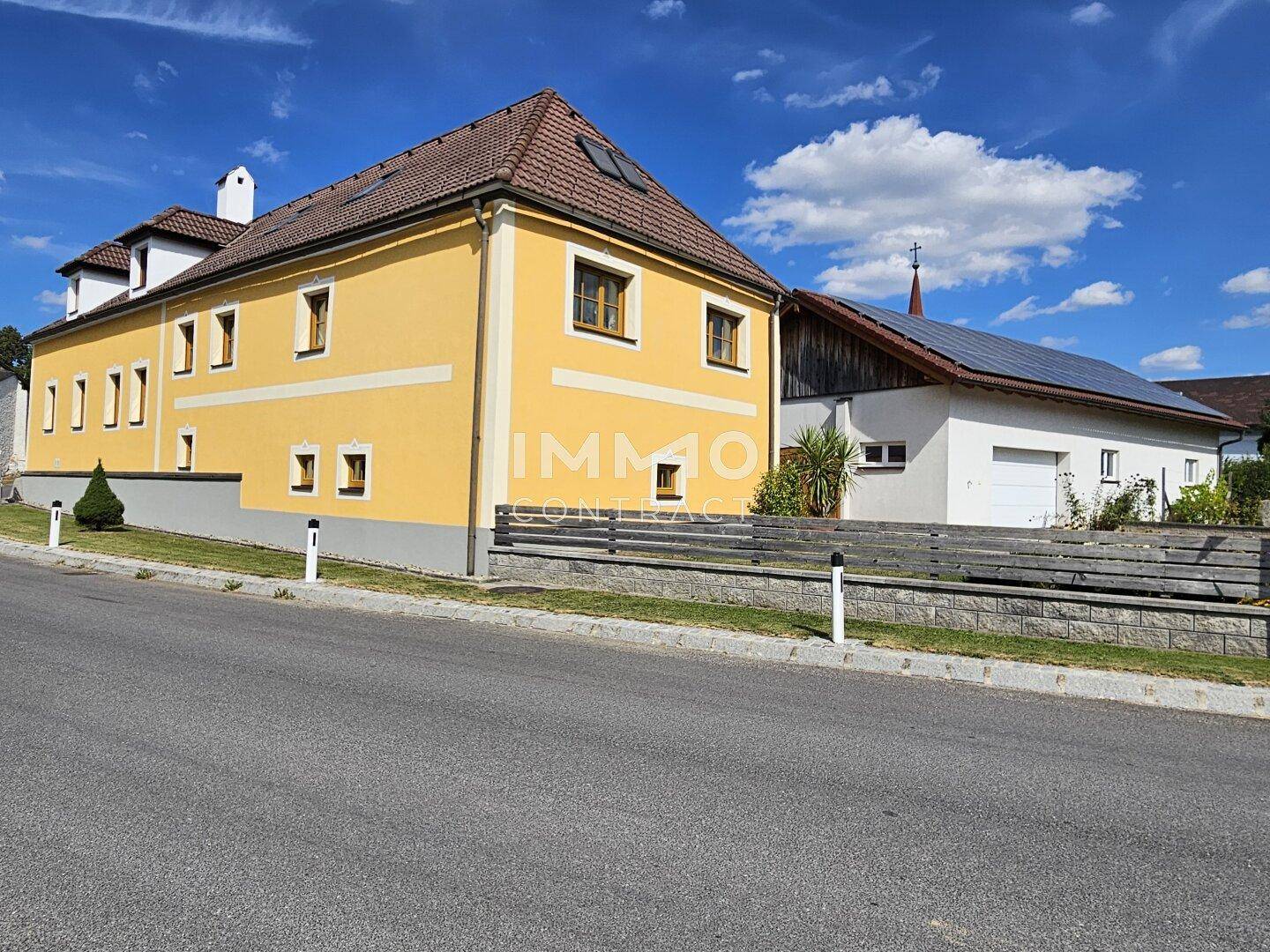 Ansicht des gelben Gebäudes von der Straße, mit einem weiteren Gebäude im Hintergrund.