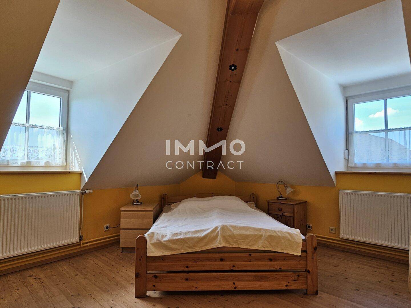 Schlafzimmer im Dachgeschoss mit Holzboden, gelben Wänden und zwei Fenstern.