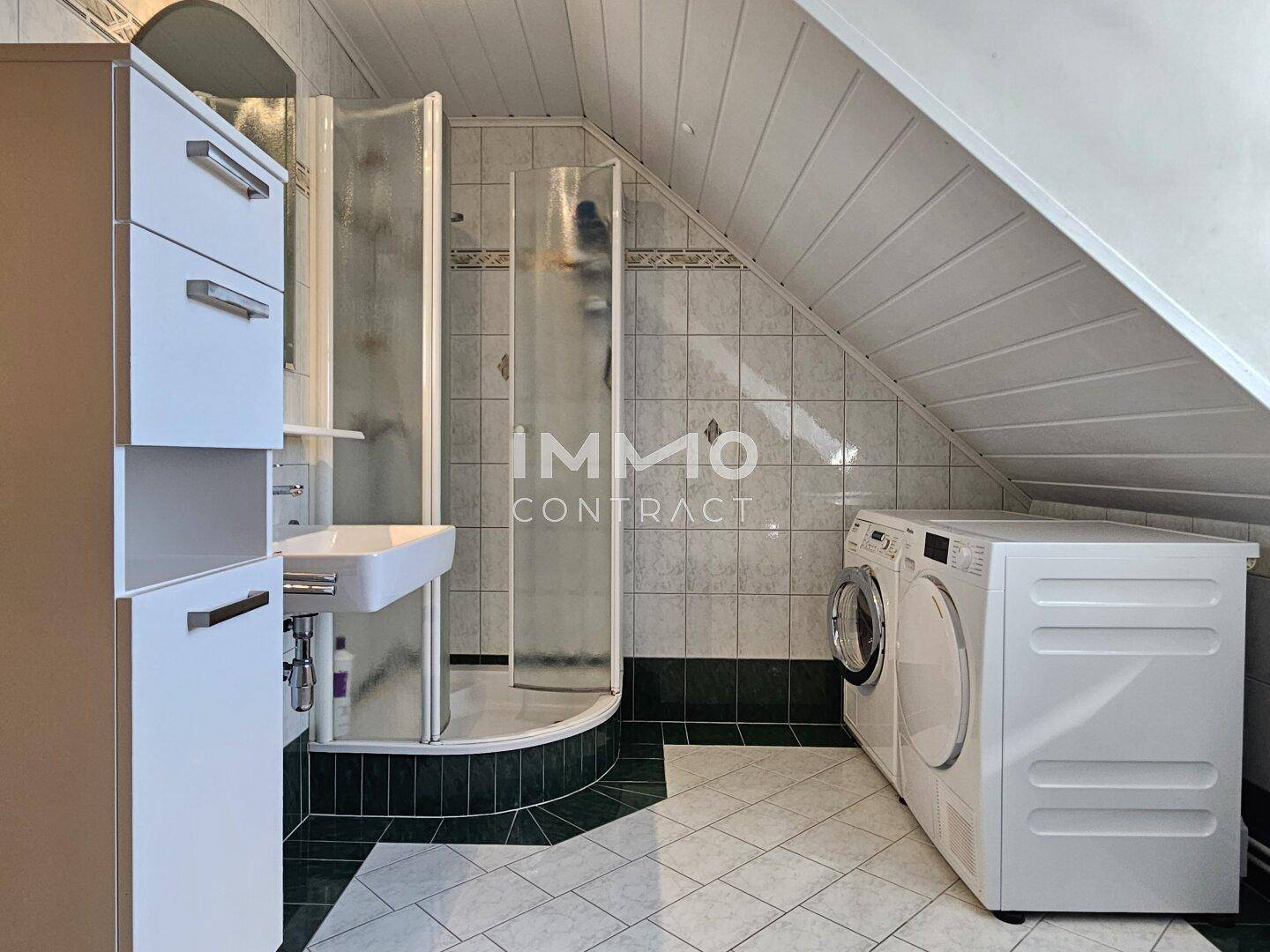 Badezimmer im Dachgeschoss mit Dusche, Waschmaschine und Fliesen in Grün- und Weißtönen.