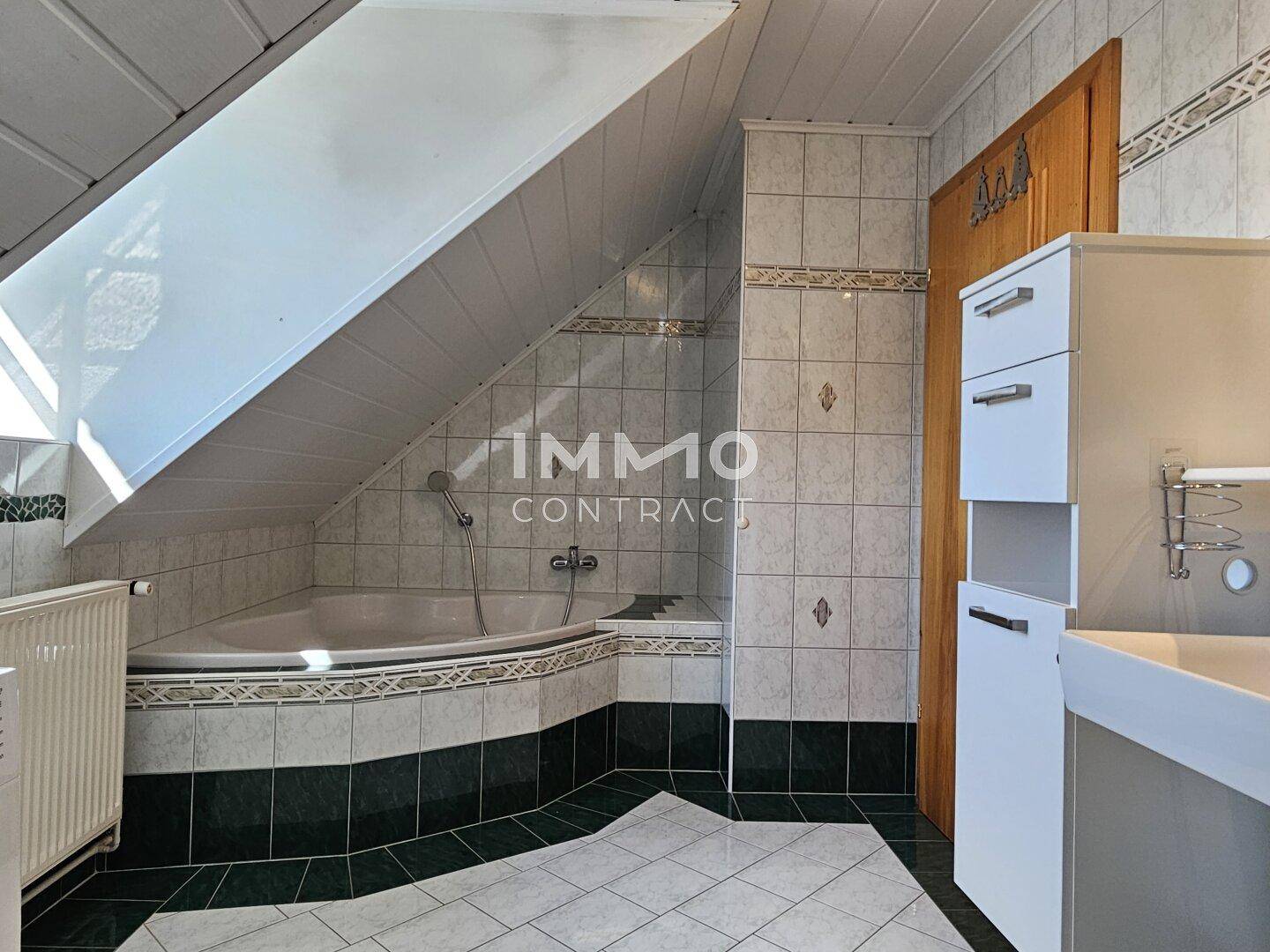 Badezimmer im Dachgeschoss mit Eckbadewanne, Fliesen und Dachfenster für natürliches Licht.