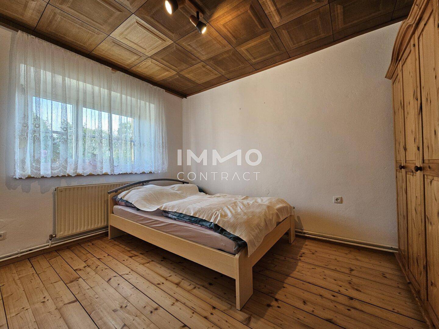 Schlafzimmer mit Holzdielenboden, Holzdecke und einem Fenster, einfach eingerichtet.