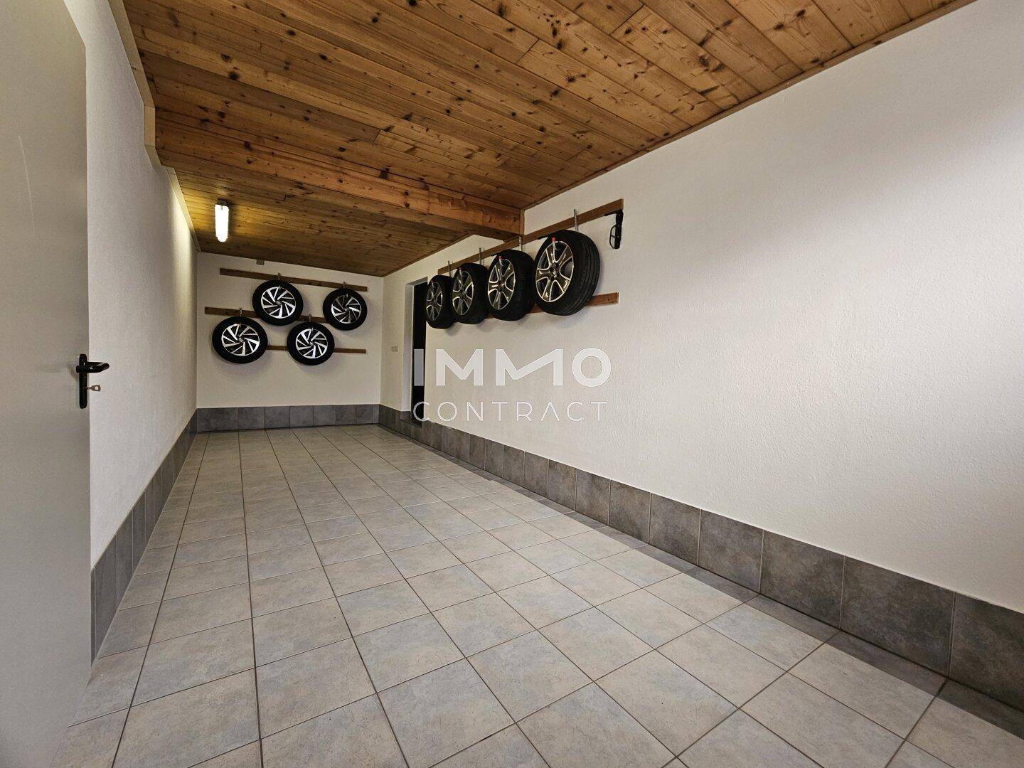 Saubere Garage mit Fliesenboden, Holzdecke und praktischer Reifenaufbewahrung an der Wand.