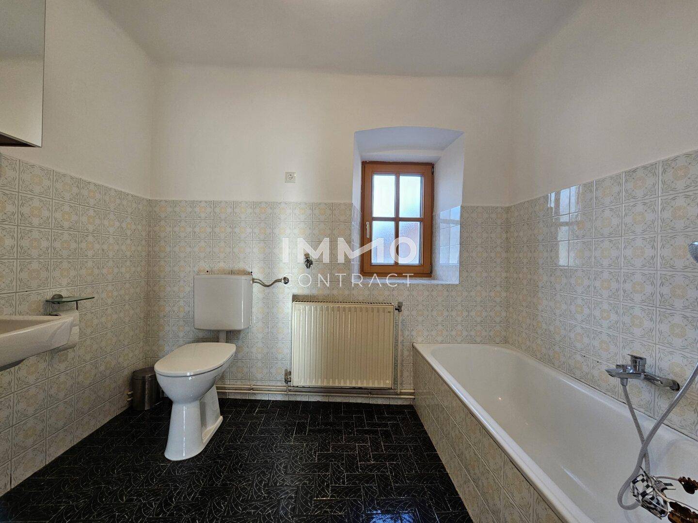 Traditionelles Badezimmer mit Badewanne, WC und gemusterten Fliesen, sowie einem kleinen Fenster.
