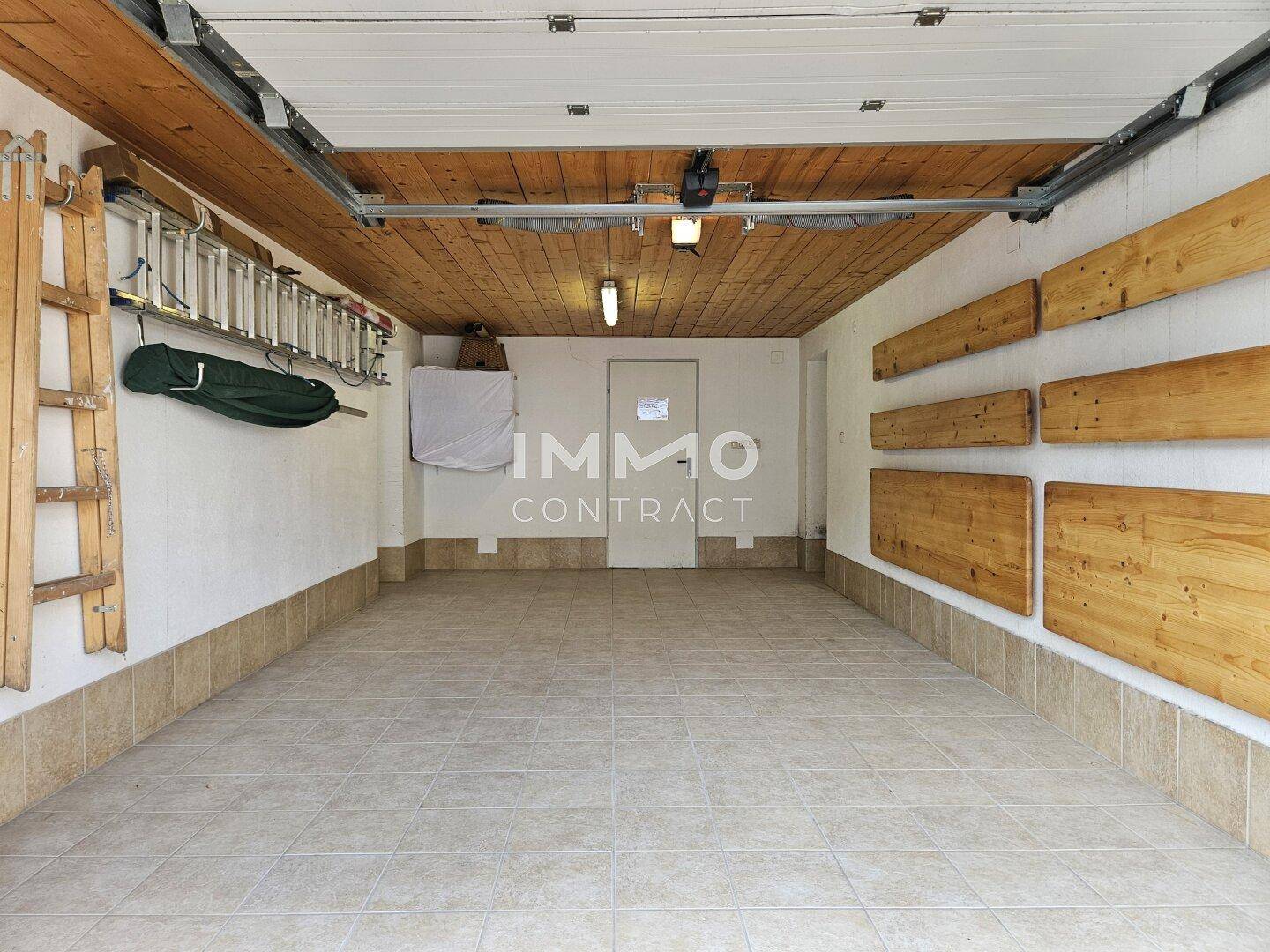 Funktionale Garage mit Fliesenboden, Holzdecke und Stauraum für Werkzeuge und Leitern.