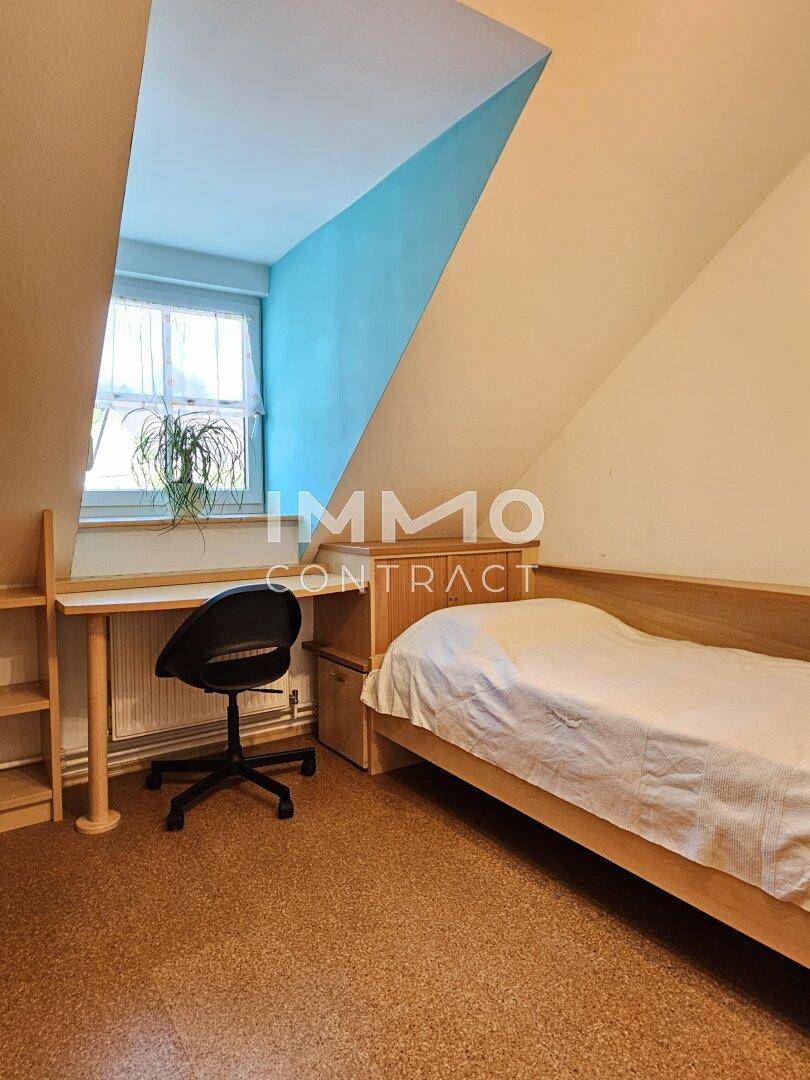 Kleines Schlafzimmer mit Holzboden, Schreibtisch und einem Fenster mit blauer Akzentwand.