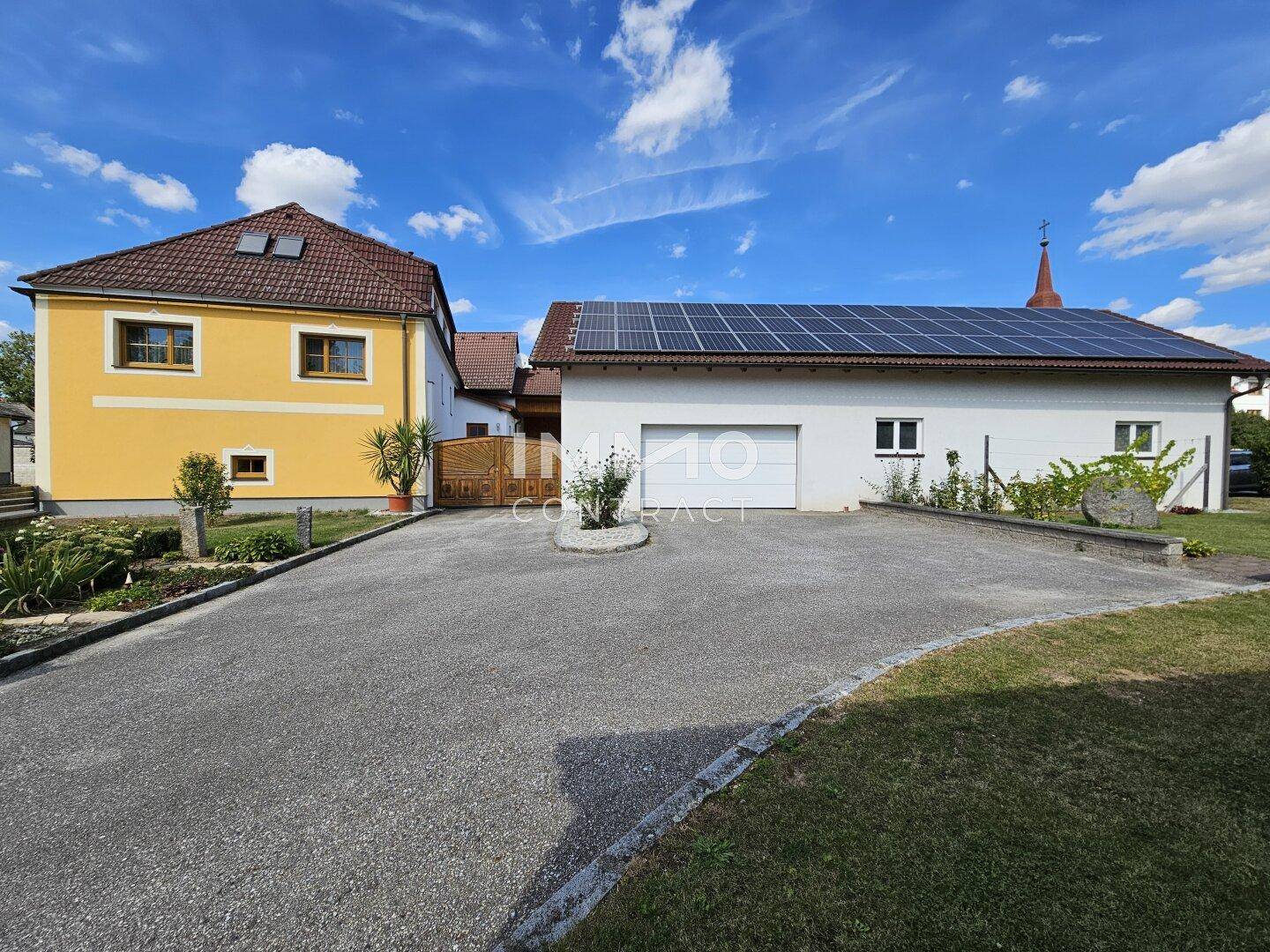 Gebäude mit Photovoltaikanlage auf dem Dach und einer breiten Zufahrt zum Garagenbereich.