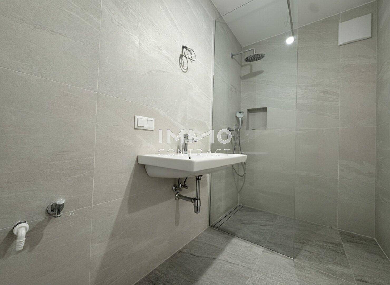 Modernes Badezimmer mit großer begehbarer Dusche, Einzelwaschbecken und hellen Fliesen.