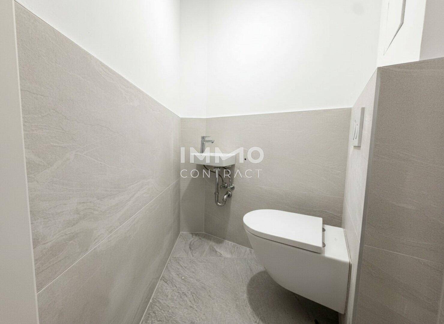 Separates Gäste-WC mit wandhängender Toilette, kleinem Waschbecken und modernen Fliesen.