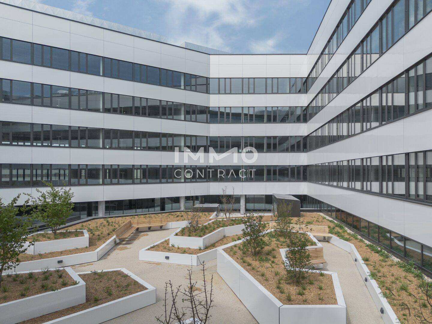 Innenhof eines modernen Bürogebäudes mit begrünten Beeten und Sitzgelegenheiten.