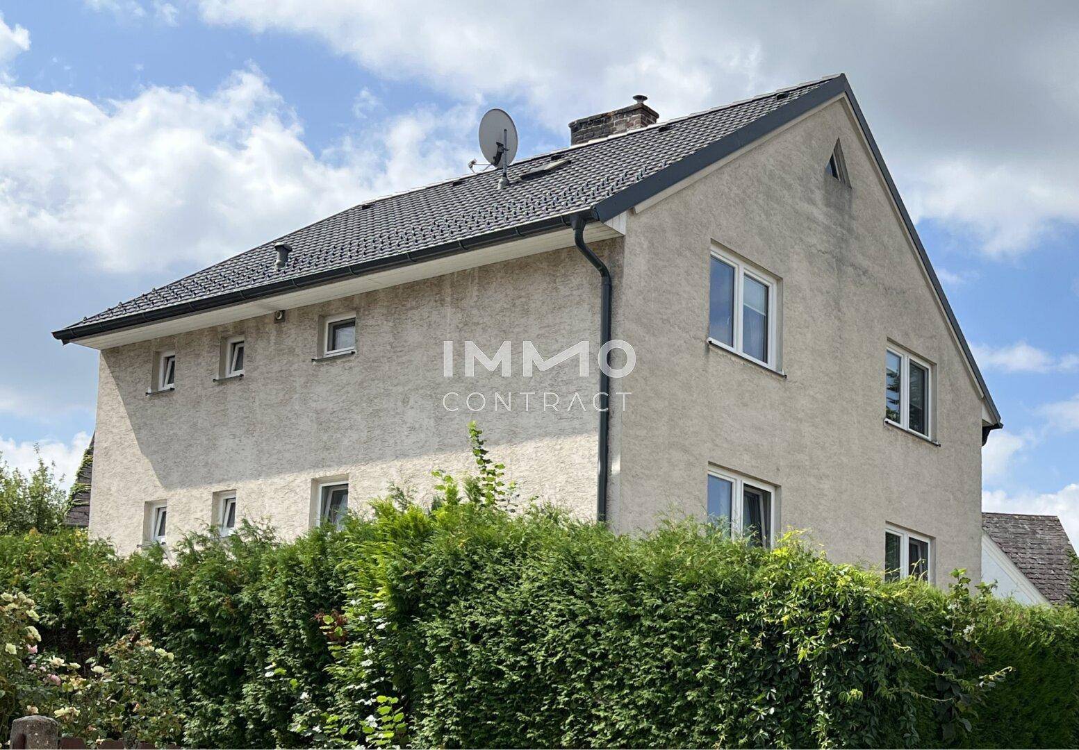 Seitenansicht des Hauses mit Satteldach und einer hohen, grünen Hecke im Vordergrund.