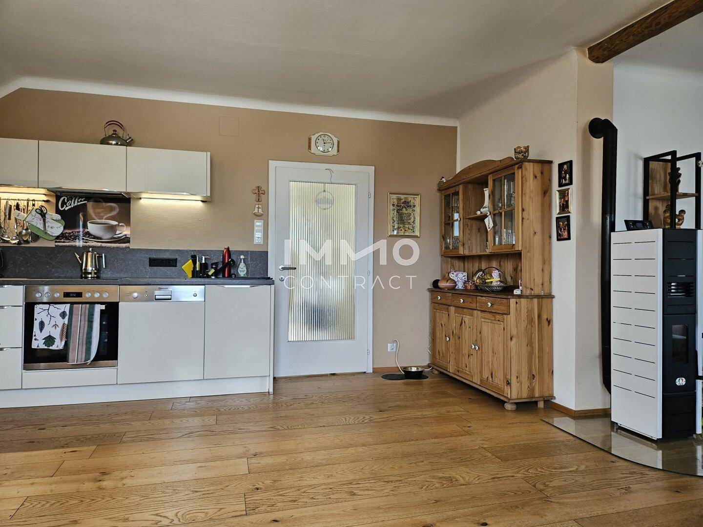 Küchenbereich mit Holzboden, weißen Schränken und einem traditionellen Holzschrank.