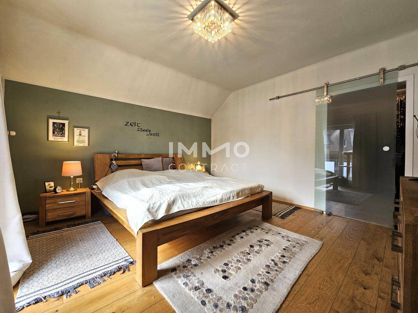Schlafzimmer mit Holzboden, Doppelbett und einer modernen Schiebetür aus Glas.