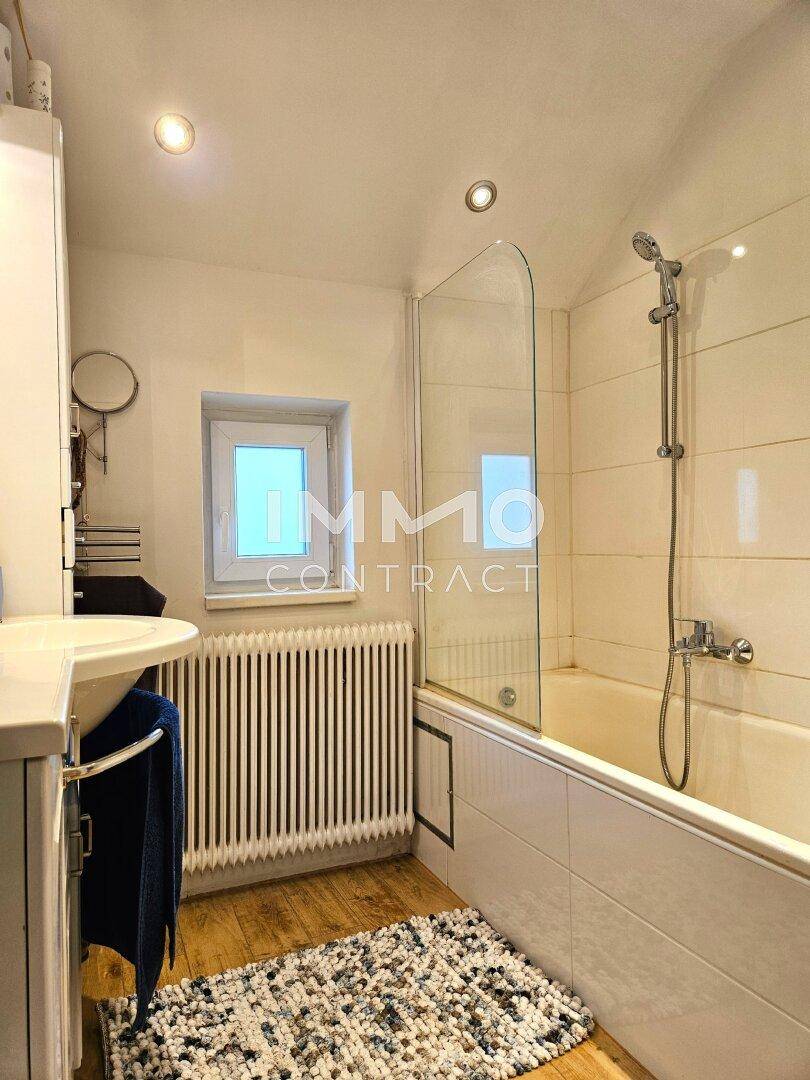 Helles Badezimmer mit Badewanne, Duschabtrennung und Fenster für Tageslicht.