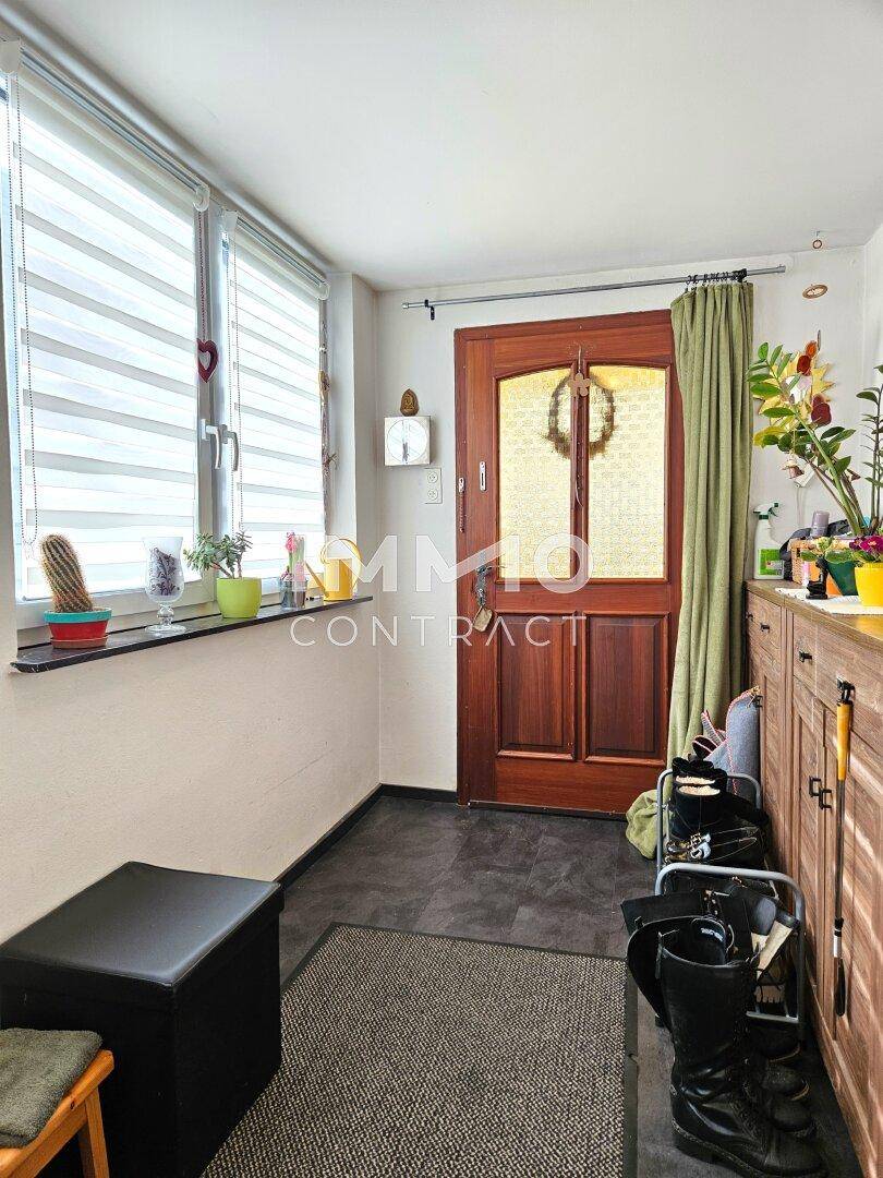 Eingangsbereich mit Fliesenboden, Fenster und einer Holztür, praktisch eingerichtet.
