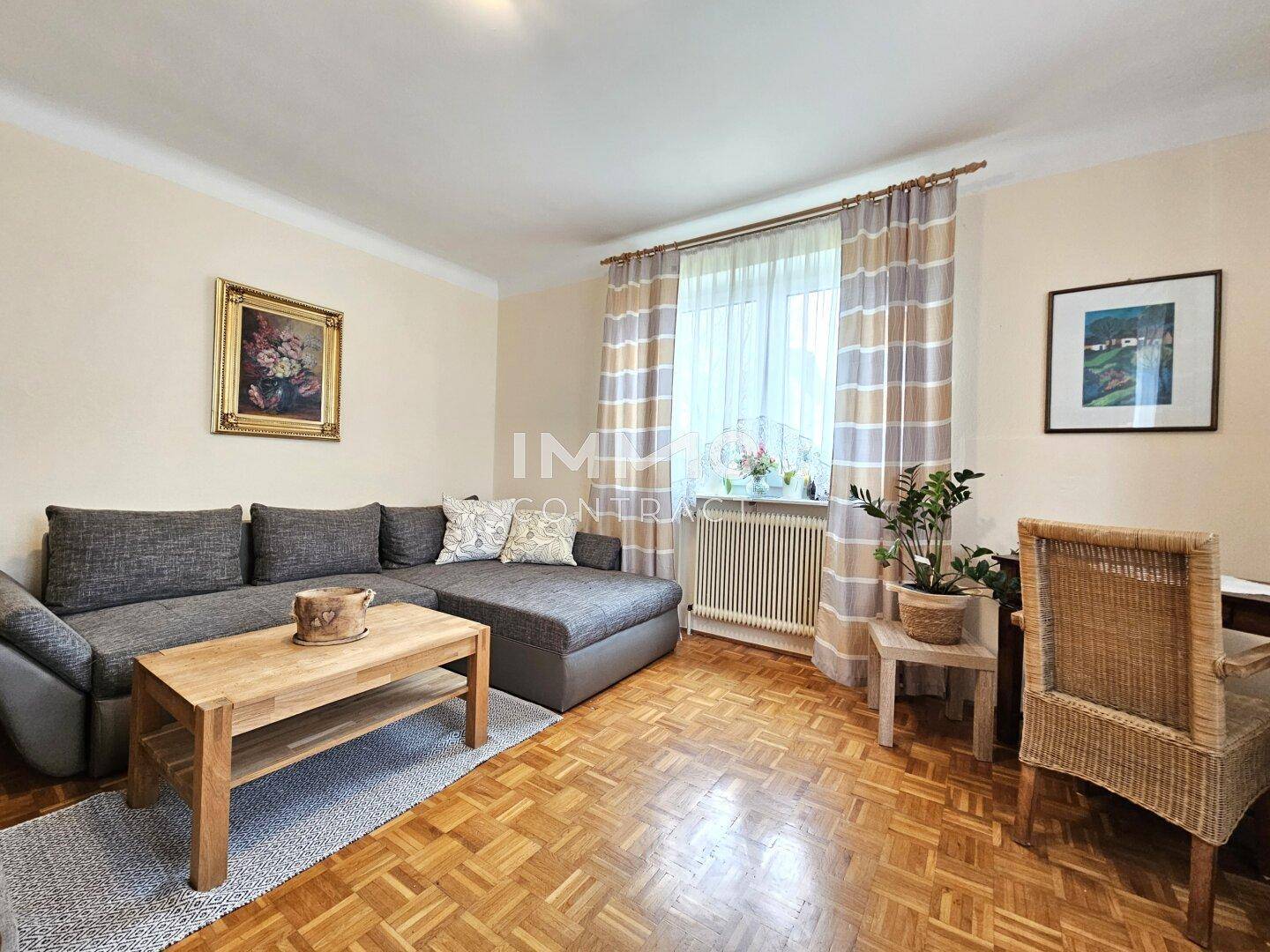 Helles Wohnzimmer mit Parkettboden, großem Sofa und einem Fenster mit Vorhängen.