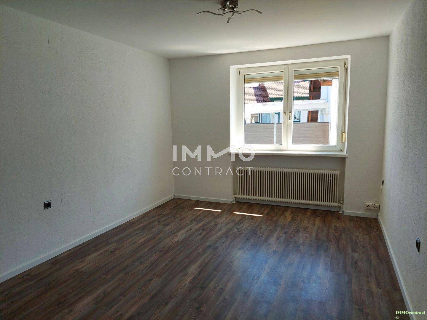 Leeres Zimmer mit Laminatboden, weiß gestrichenen Wänden und einem Fenster.