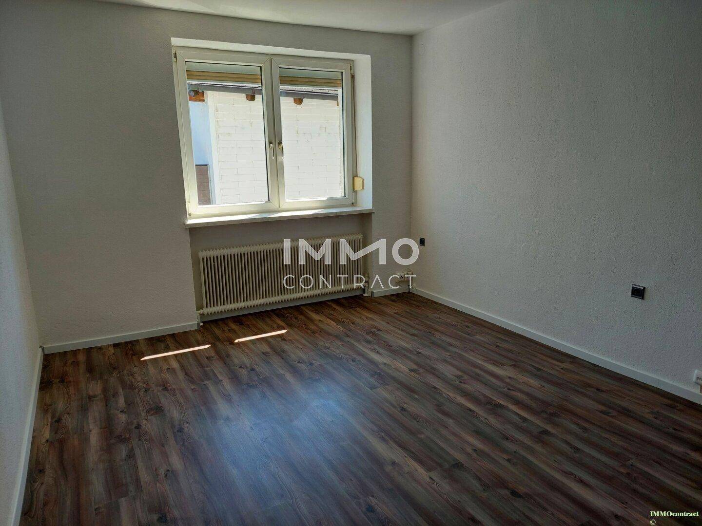 Helles Zimmer mit Laminatboden, weiß gestrichenen Wänden und einem großen Fenster.