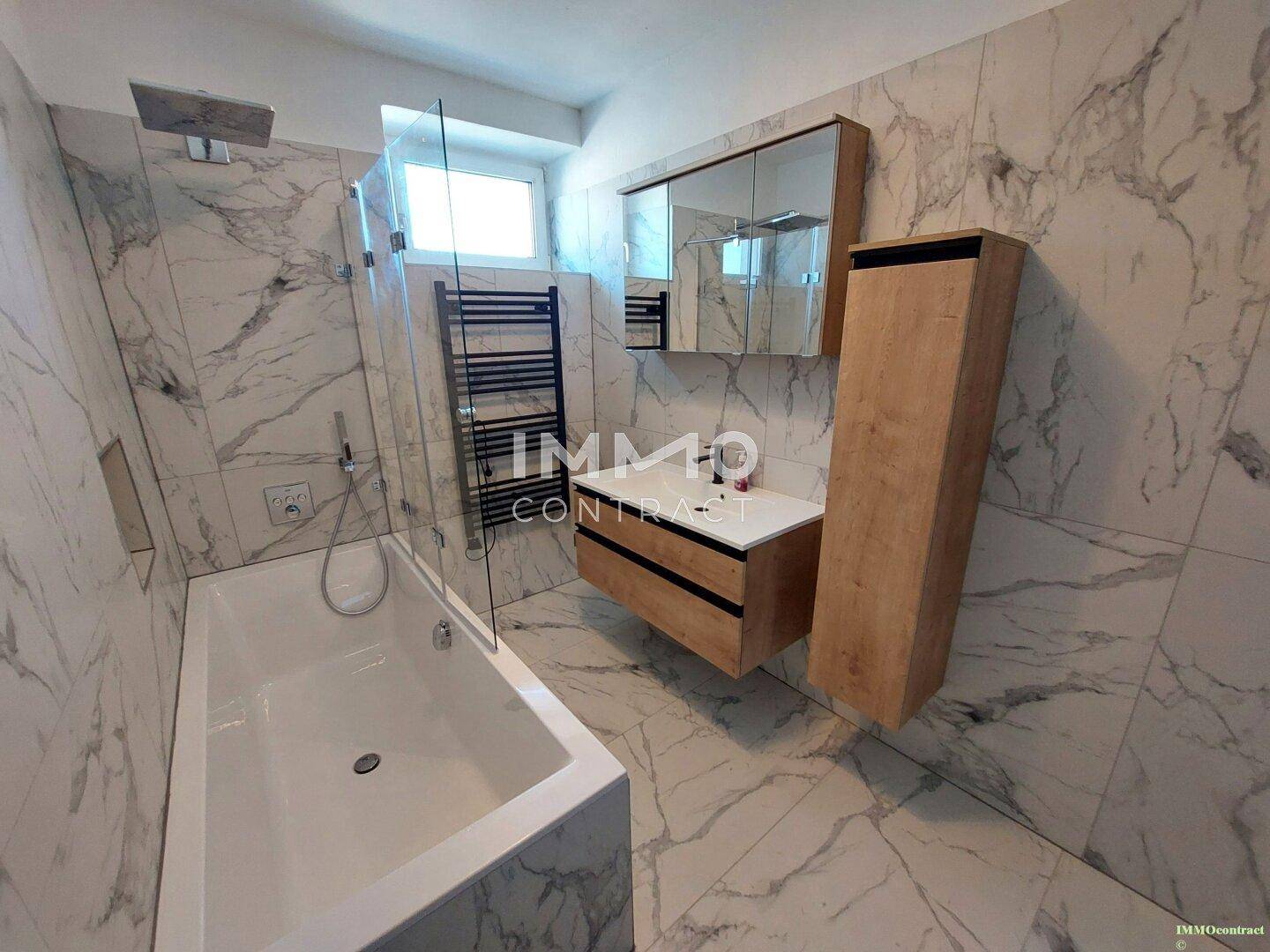 Modernes Badezimmer mit Marmorfliesen, Badewanne, Waschtisch und beheiztem Handtuchhalter.