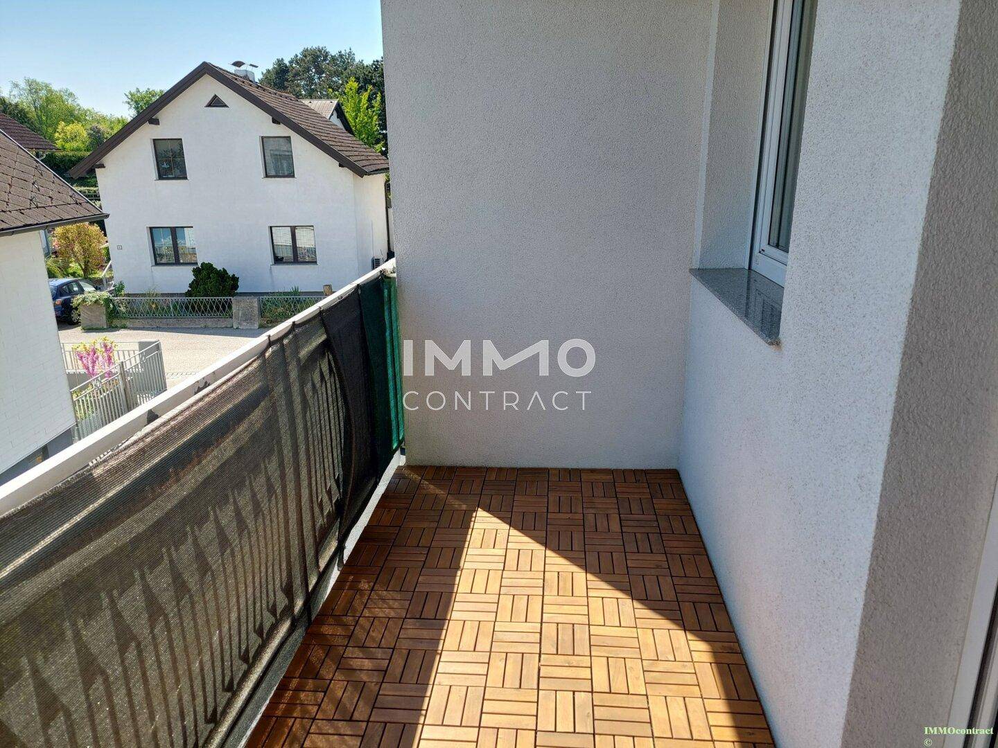 Kleiner Balkon mit Holzbodenfliesen und Blick auf die umliegenden Häuser.