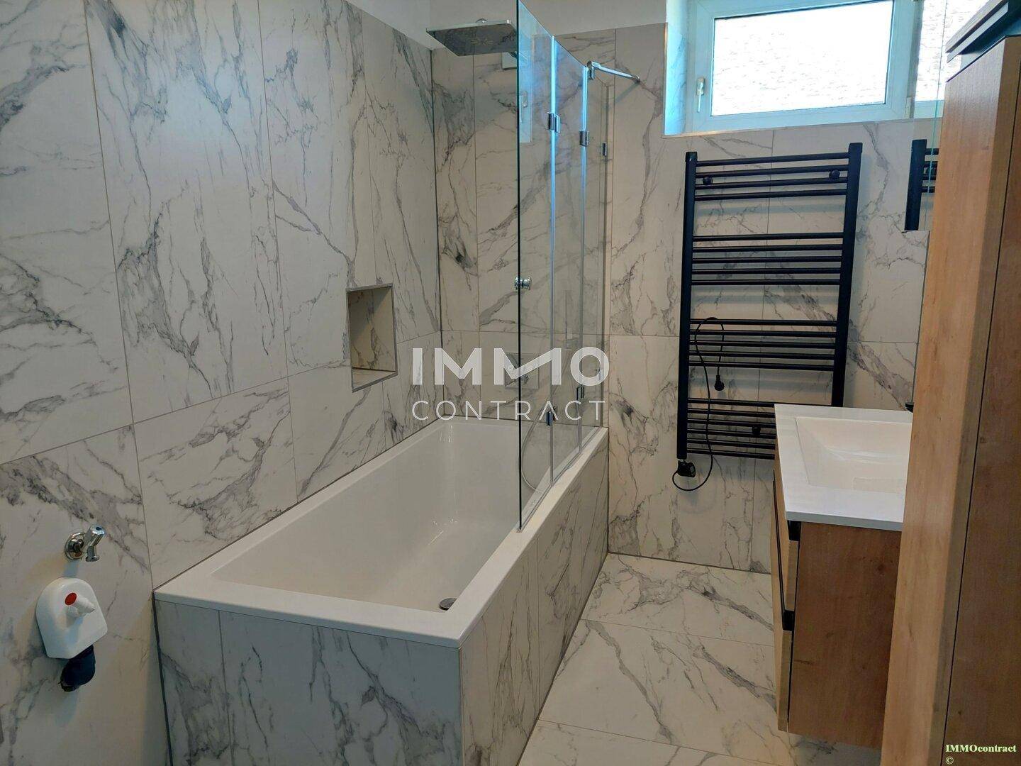 Modernes Badezimmer mit eleganten Marmorfliesen, Badewanne und beheiztem Handtuchhalter.