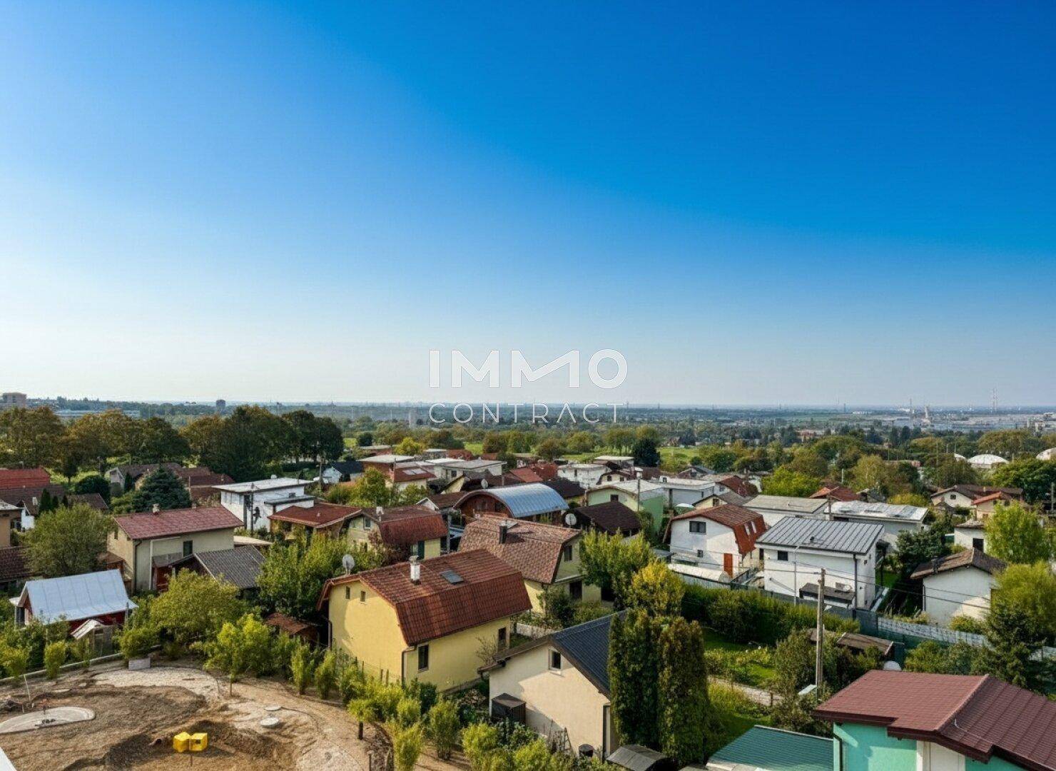 Weitläufiger Blick über eine Wohnsiedlung mit vielen Häusern und grünen Bäumen unter klarem Himmel.